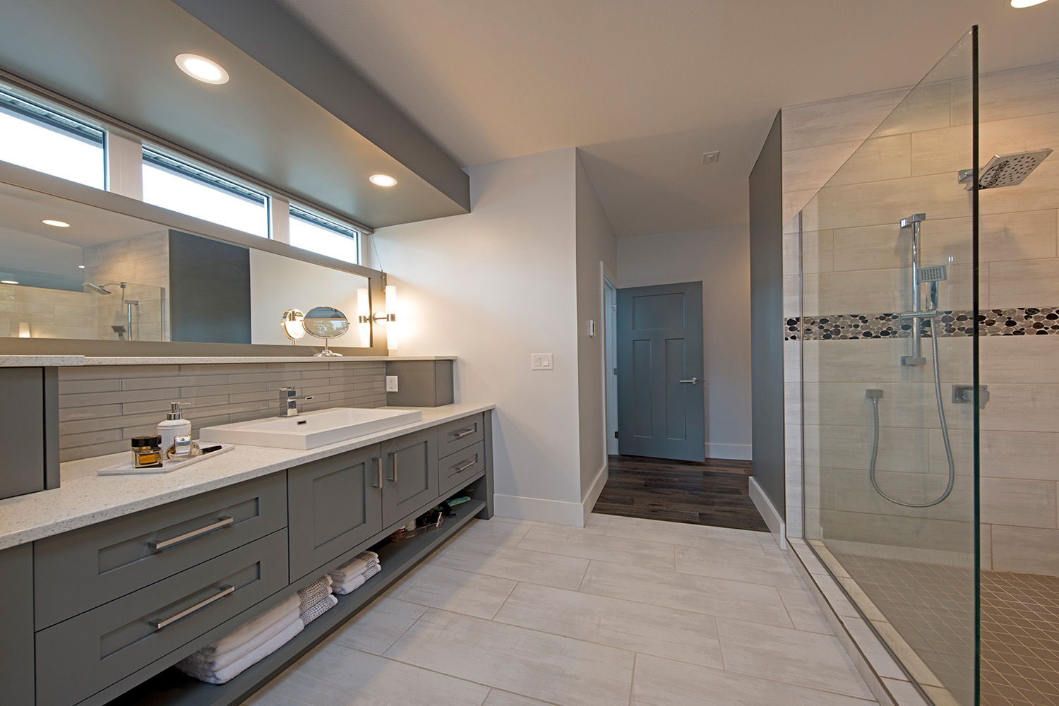 spacious modern bathroom with white tile and grey cabinets, thin skylight window and rain shower