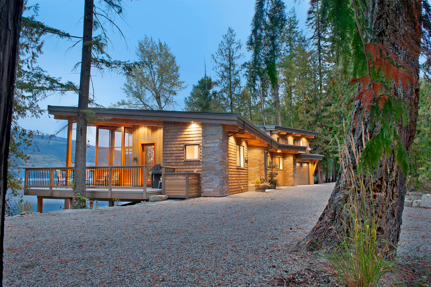 lake view home with rock tile pillars and surrounding forest