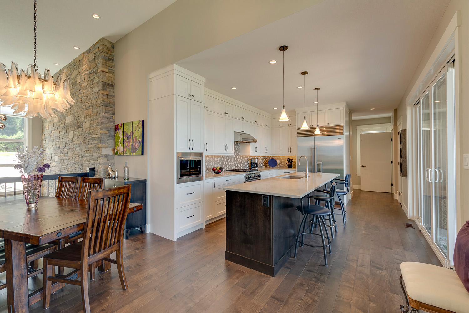 Open concept kitchen and dining space hanging light fixtures, and rock tile wall accents