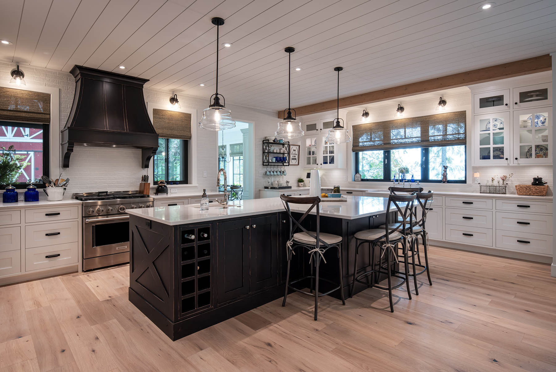 A spacious kitchen with a modern design, featuring white cabinetry, black accents, a large central island with seating, and hardwood floors.
