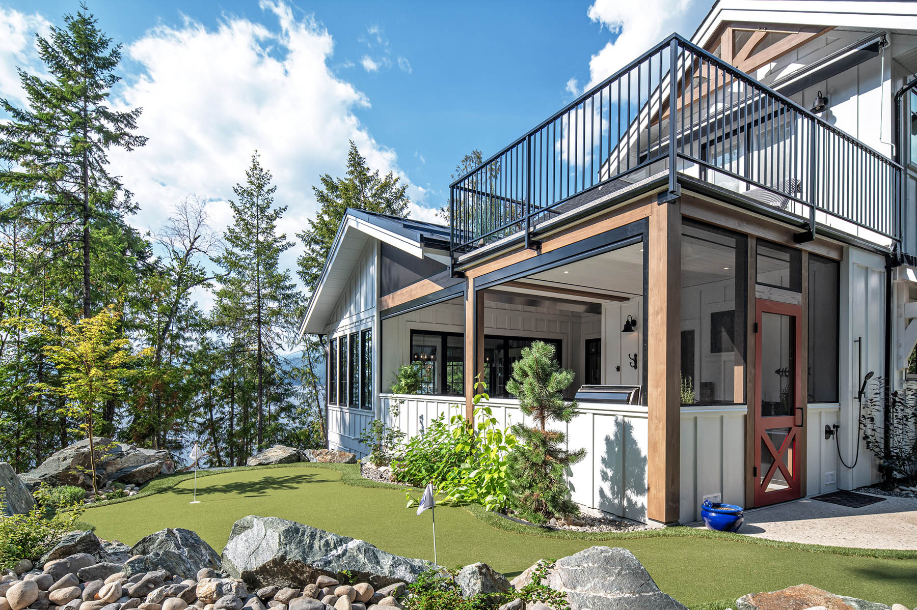 Modern hillside home with a compact personal putting green, surrounded by natural rocky landscaping and lush greenery, offering an invigorating view of a forested area.
